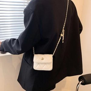 White quilted crossbody bag with gold camellia logo and metal chain on black blazer