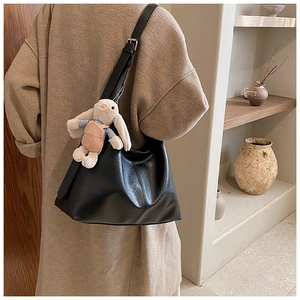 Detailed view of black textured leather tote bag with cute plush bunny charm on a model