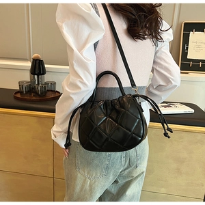 Detail showing a black quilted bucket bag with a top handle on a person's shoulder