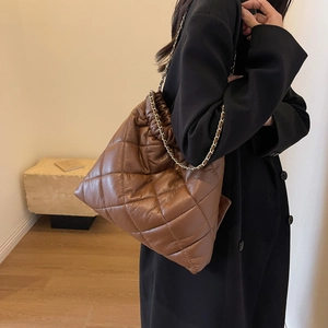 Detail of a brown quilted tote bag with chain strap worn by a model in a minimal room