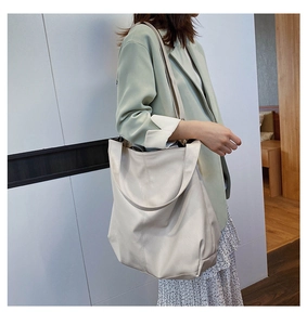 Detail of a large creamy white tote bag with long straps on a model in a blazer