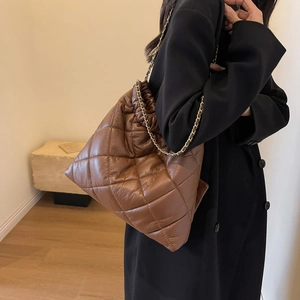 Detail view of brown quilted tote bag with glossy finish and elegant gold chain strap