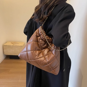 Detail view of brown quilted puffer tote bag with golden chain strap on a model