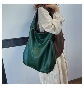 Detail shot of a large dark green hobo bag with a soft leather texture on a female model