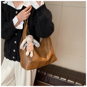 Detail of a large brown shoulder tote bag featuring a cute bunny plush charm on a strap