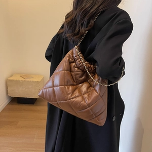 Close-up of brown quilted tote bag with gold chain strap worn over a black coat