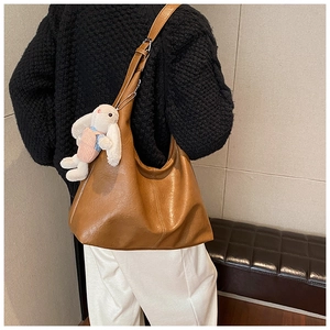 Detail of a large brown shoulder tote bag with a cute plush rabbit charm on the side