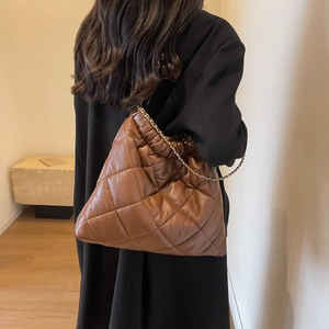 Close-up of brown quilted leather tote bag with metal chain strap on model shoulder