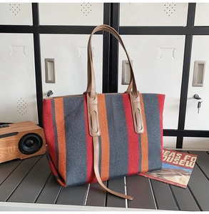 Detail of red and orange striped canvas tote with brown leather handles on a modern cabinet