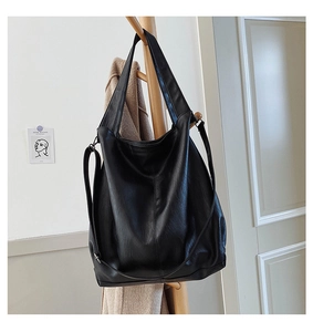 Detail of a large black leather tote bag hanging on a rack with a removable strap