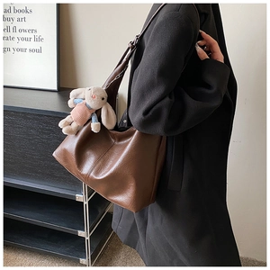 Detail of dark brown tote bag on shoulder with cute plush rabbit keychain accessory