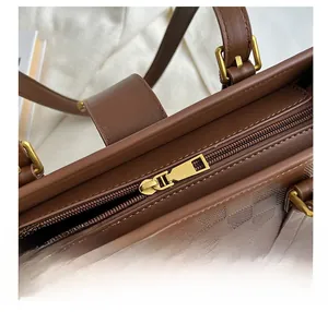 Close-up of smooth gold zipper hardware on brown checkered embossed leather tote bag