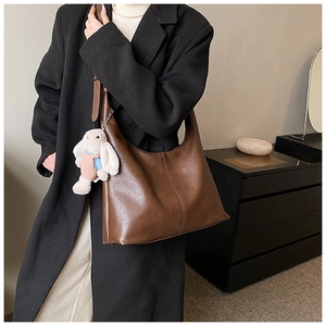 Detail of dark brown matte leather tote bag with a cute plush rabbit charm on the shoulder