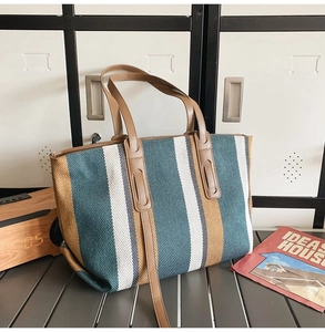 Close-up of a large striped canvas tote bag with brown leather handles in a chic setting