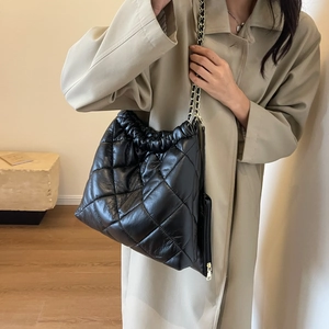 Quilted black tote bag with gold chain strap shown on model wearing trench coat