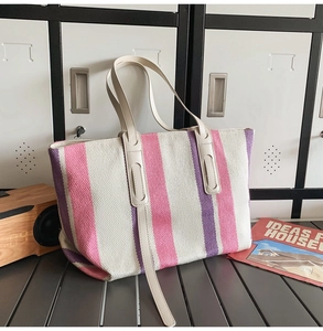 Detail of pink and purple striped canvas tote bag showing stitching and leather handles