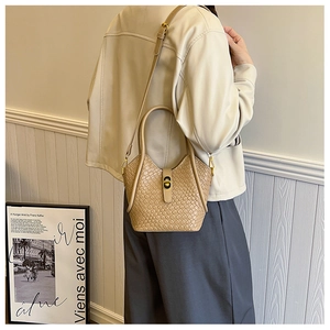 Détail d'un sac seau tissé beige montrant la bandoulière réglable et le fermoir en métal