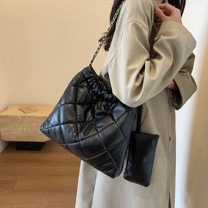 Detail of black quilted tote bag with drawstring closure and metal chain strap