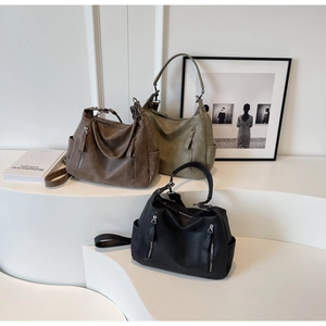 Three large soft leather tote bags in brown, green, and black on minimalist white stairs
