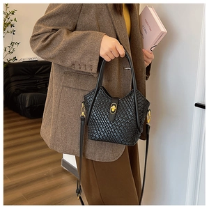 Détail d'un sac bandoulière tressé noir avec fermoir doré et veste à chevrons marron