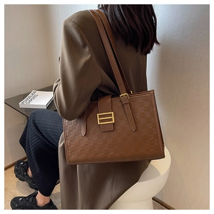 Detail of a brown checkered tote bag with adjustable straps and golden hardware buckles
