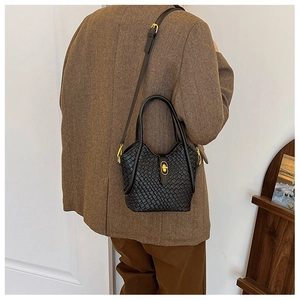 Détail d'un sac seau tressé noir avec garnitures dorées porté avec un blazer marron