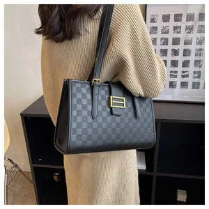 Detail of black checkered tote bag with gold buckle and shoulder straps on a model