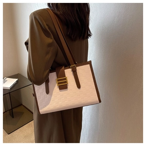 Detail of cream tote bag featuring embossed grid texture and brown leather trim details