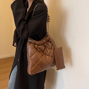 Detail of a brown quilted tote bag featuring a gold chain strap and drawstring closure