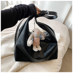 Detail of black textured leather tote bag with cute plush rabbit charm and wide strap