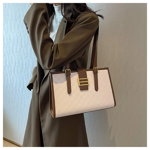 Close-up of white tote bag with brown trim and gold buckle on a model's shoulder