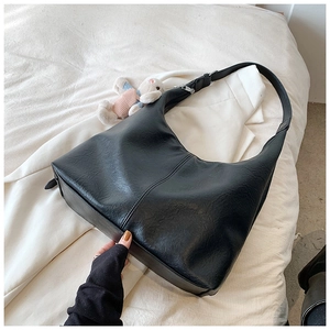 Detail of black faux leather tote bag with vertical stitching and rabbit doll charm