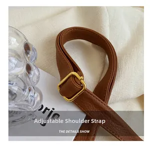 Detail of adjustable brown pebbled leather shoulder strap with square gold metal buckle