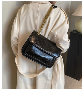 Close-up of black chevron quilted glossy leather bag with golden sliding chain strap