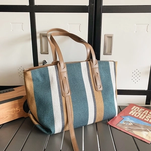 Large striped canvas tote bag with brown handles on a modern minimalist desktop