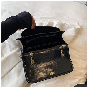 Detail view of the black glossy bag showing multiple interior compartments and gold chain
