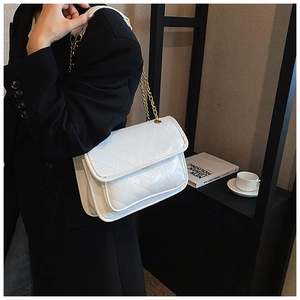 Close-up of a white quilted crossbody bag with a gold chain strap on a black blazer