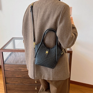 Sac seau tressé noir tendance avec détails dorés porté en bandoulière par un mannequin