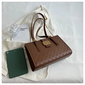 Detail of a brown checkered tote bag with gold hardware and embossed texture