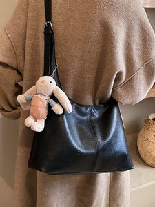 Minimalist black oversized tote bag with a cute rabbit pendant worn over a brown coat