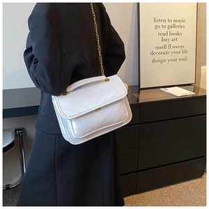 Close-up of white V-quilted crossbody bag with gold chain strap on black blazer