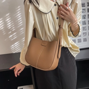 Detail of tan pebble leather bucket bag with adjustable strap and embossed flap closure