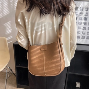 Brown lychee leather shoulder bag with adjustable strap in a minimalist office setting
