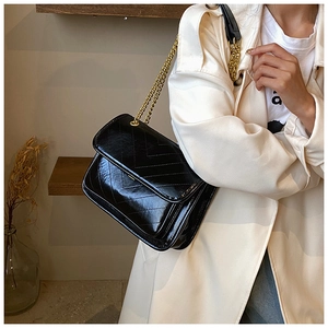 Detail of a black V-quilted chain shoulder bag worn with a stylish white trench coat