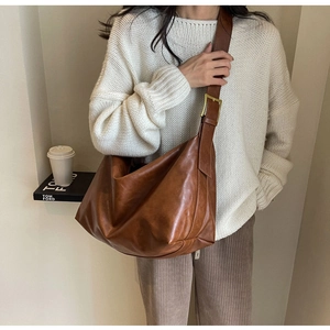 Detail van een bruine grote hobo tas met een gouden metalen gesp en brede schouderriem