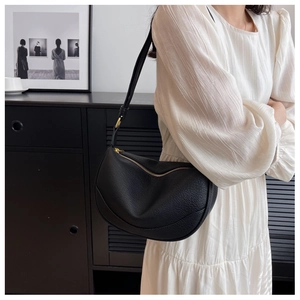 Detail of black litchi grain leather crescent bag with gold zipper on a model