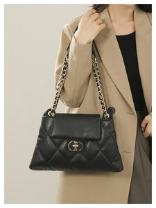 Detailed close-up of quilted black leather texture and gold metal chain strap on a tote bag