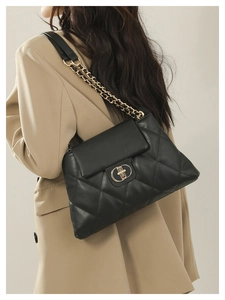 Detail of black quilted shoulder bag with gold chain strap and metal lock on beige blazer