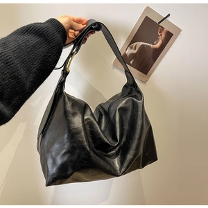 Detailopname van een zwarte zachte leren shopper met een gouden gesp en brede schouderband