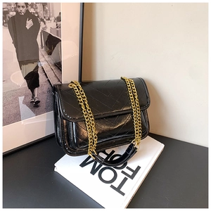 Detail of black chevron quilted shoulder bag with golden chain strap on a white book